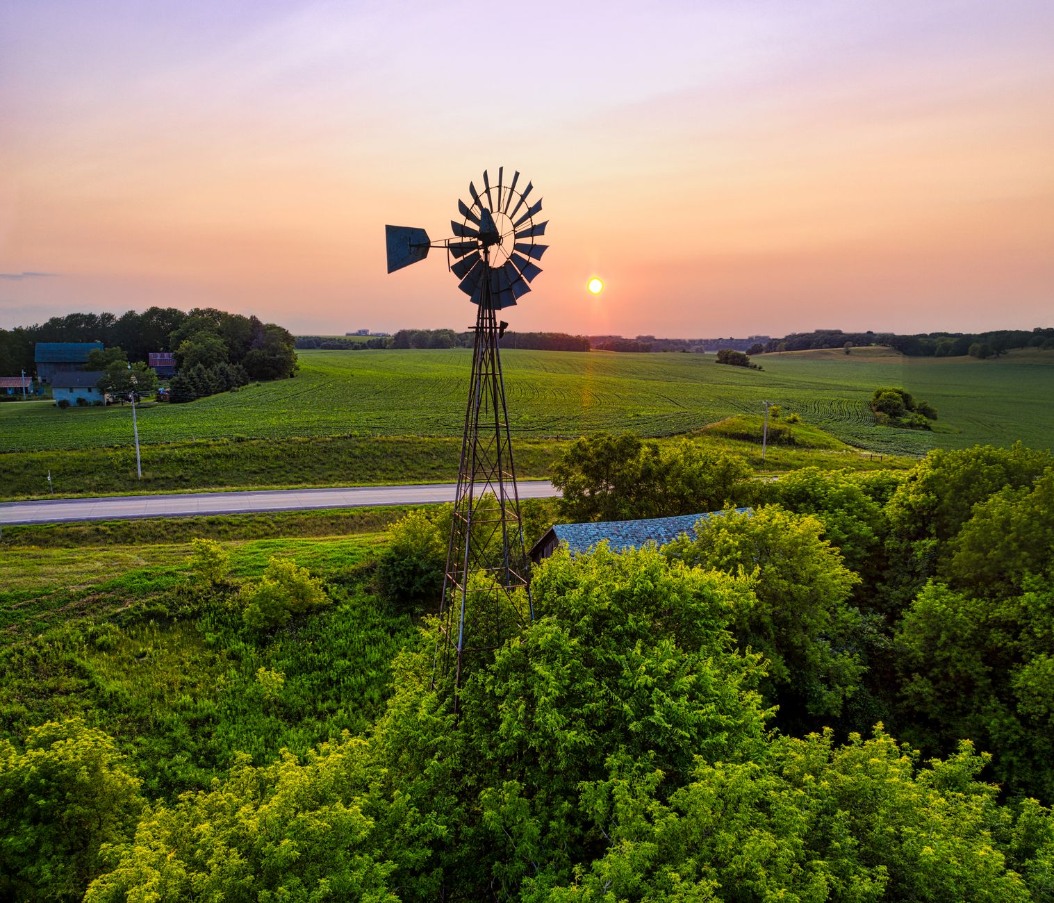 A small three blade wind turbine on a lattice tower above green pasture