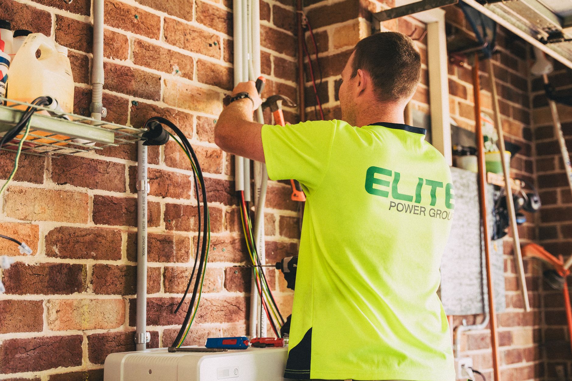 White home battery unit mounted on a garage wall next to a breaker panel
